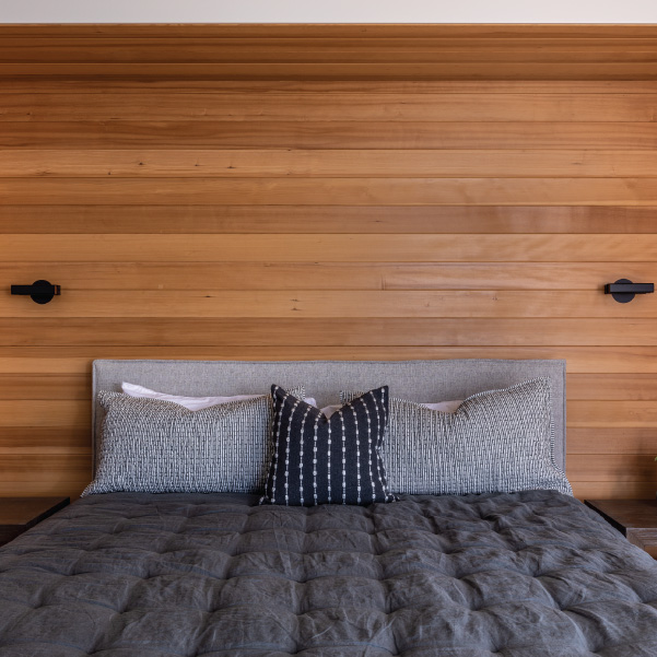 A bed with pillows in front of horizontal paneled wall with scones