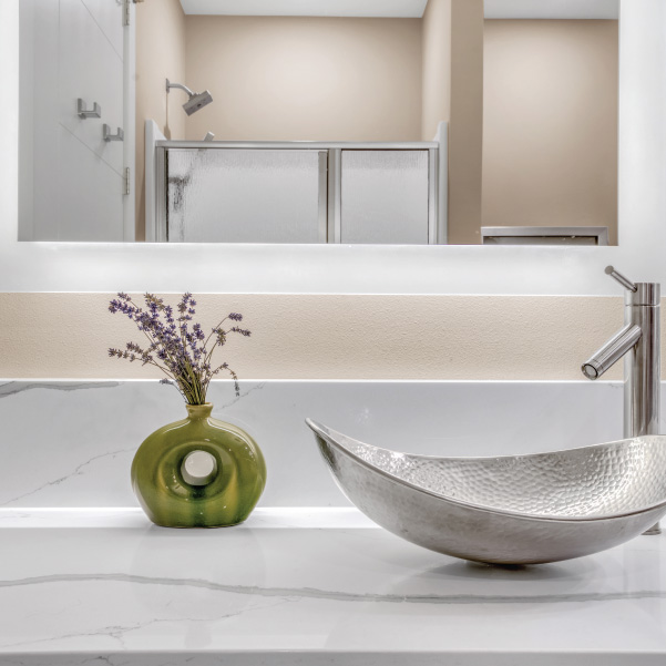 Silver metallic sink on a marble countertop under mirror with reflection of a modern shower