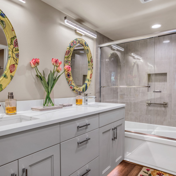 Double vanity with floral framed mirrors along full-sized bath and shower