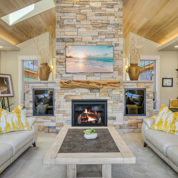 A flooring-to-ceiling fireplace with a mounted painting and wood mantle in a custom home built by Mike Riddle Construction