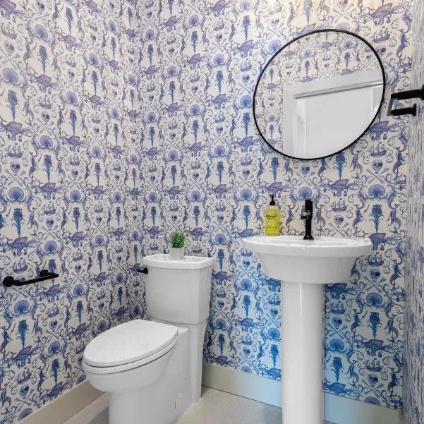 Blue and white powder room with pedestal sinks and oval mirror